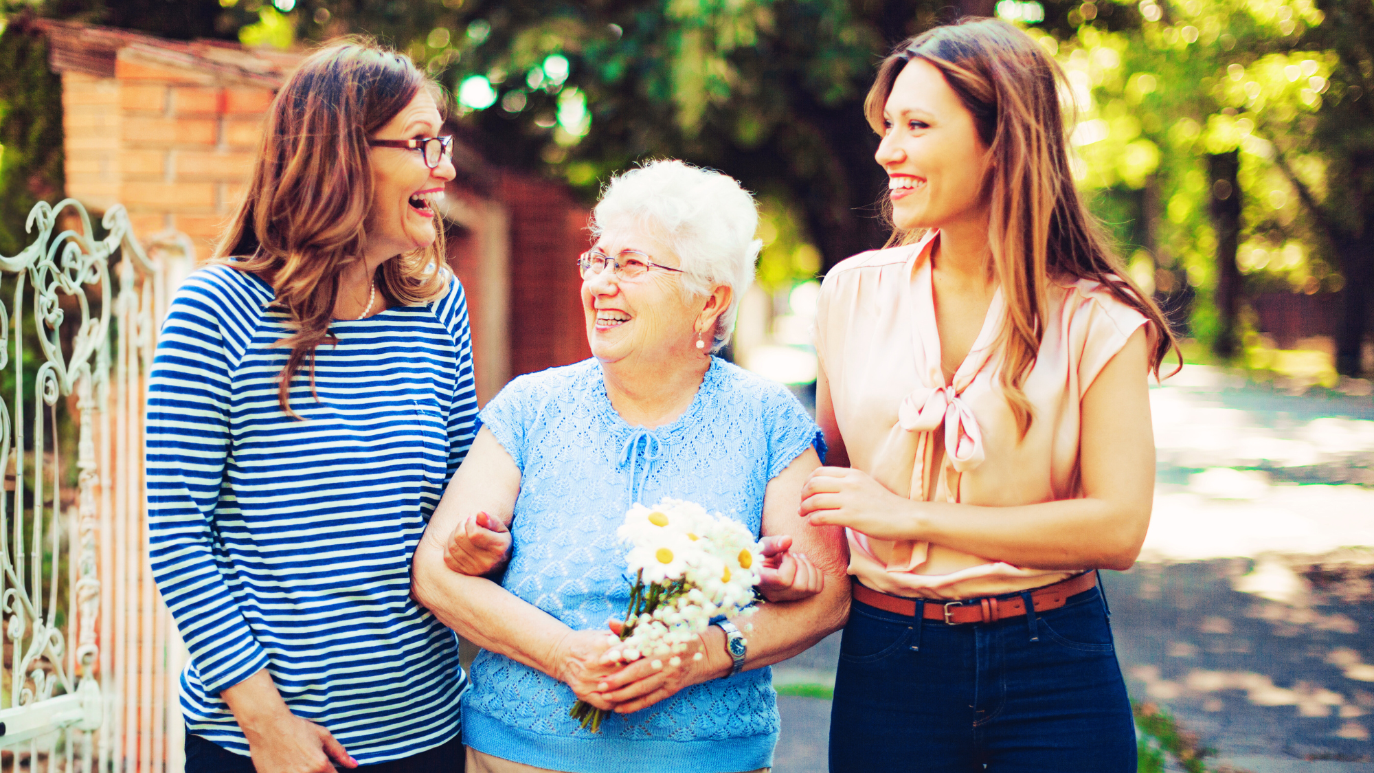 laughing senior woman holding daisies walking with daughter and granddaughter