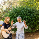 team member and elderly person dancing and playing guitar