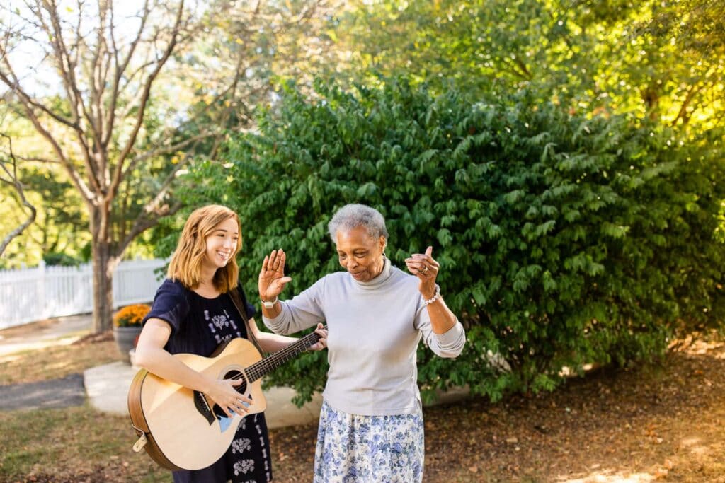 team member and elderly person dancing and playing guitar