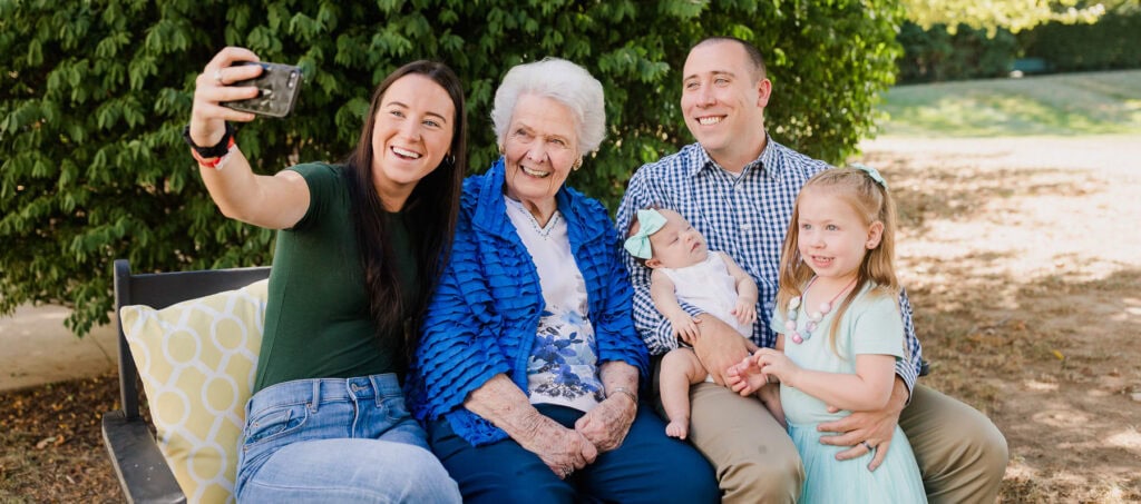 young family with children taking selfie with elderly woman on park bench