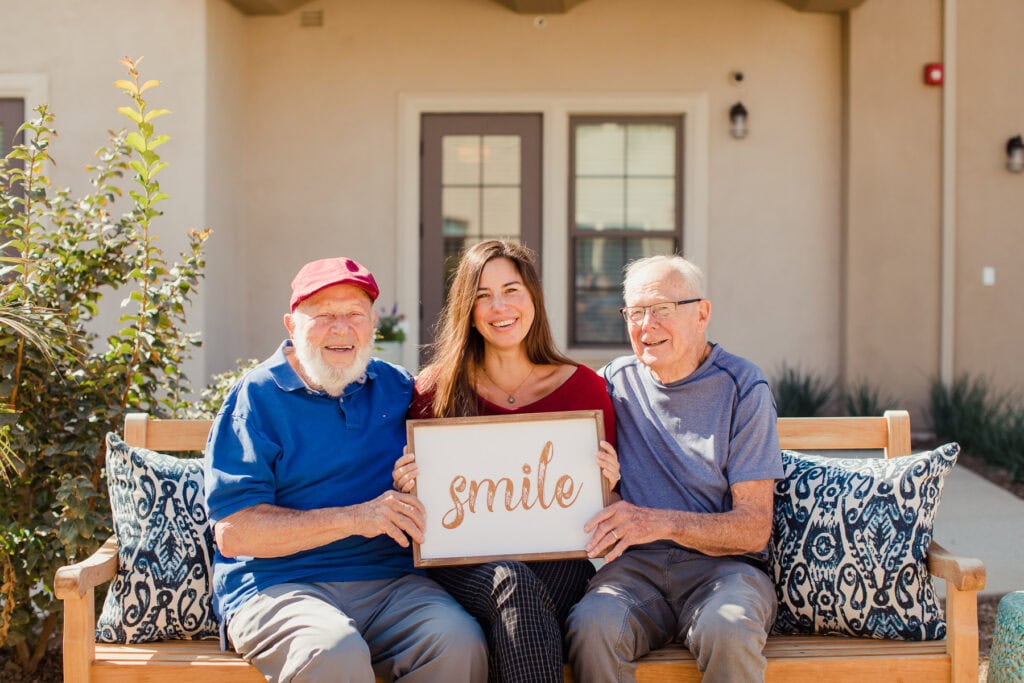 two older men sitting with young woman holding sign that says smile